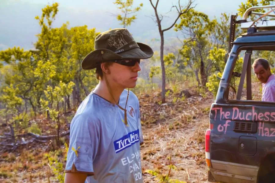 Team member in an Elephant Charge 2010 shirt next to a Land Cruiser in the bush