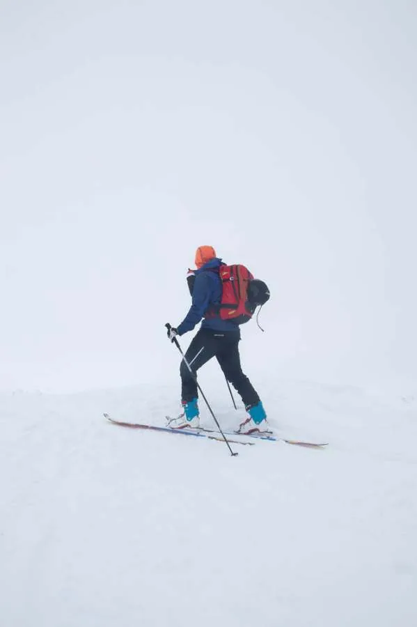 Original shot: a ski tourer with a red backpack climbing into flat white fog