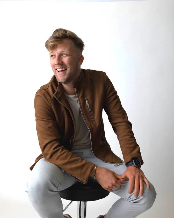 Alex Bowen, creative producer from Salzburg, Austria, laughing on a studio stool