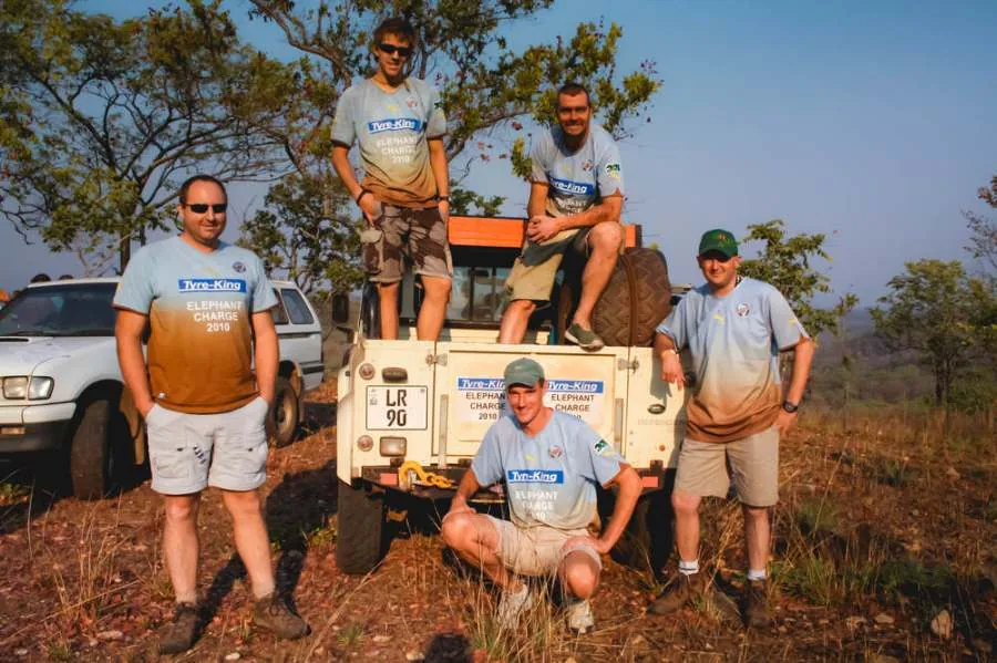 Five team members in matching Elephant Charge shirts posing with their Land Rover